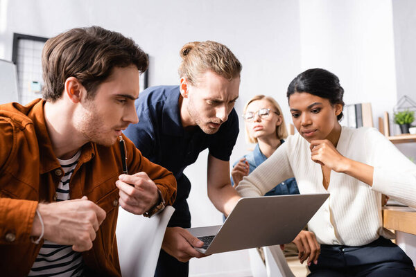 young man holding laptop near thoughtful multicultural businesspeople