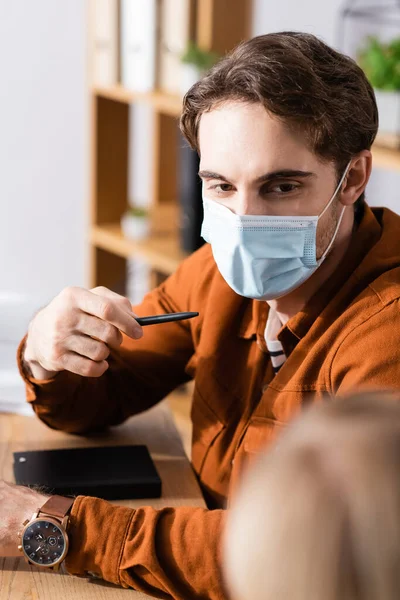 Gerente Máscara Médica Apuntando Con Pluma Mientras Está Sentado Lugar —  Fotos de Stock