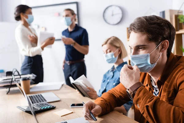 Young Businessman Fixing Medical Mask Face While Working Colleagues Blurred — Stock Photo, Image