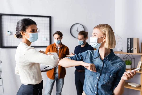Młodzi Menedżerowie Maskach Medycznych Wykonujący Gest Uderzenia Łokciem Pobliżu Biznesmenów — Zdjęcie stockowe