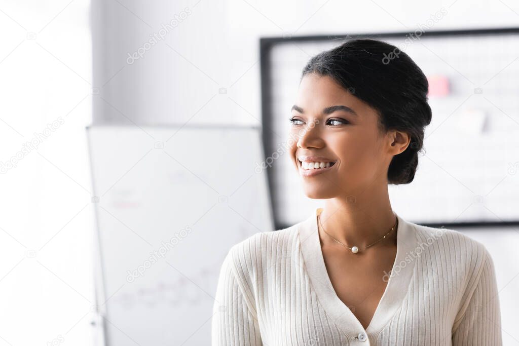 Happy african american woman looking away while standing in office on blurred background