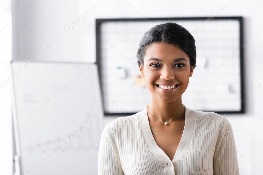 Smiling african american woman looking away while standing in office on blurred background