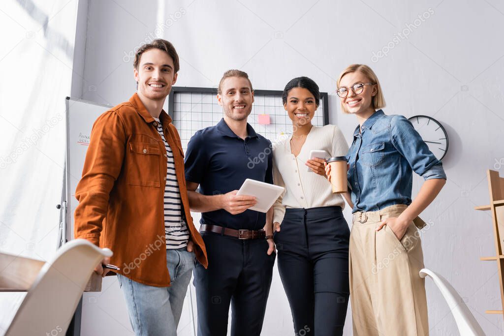 happy, young multicultural businesspeople looking at camera in office