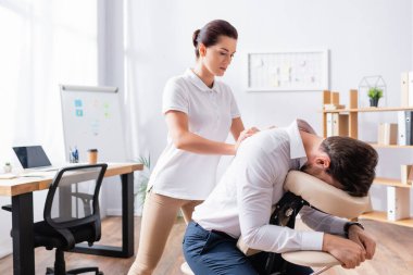 Masseuse doing seated massage of businessman back in office clipart