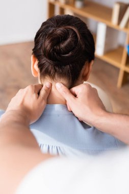 Back view of massage therapist massaging neck of female client on blurred foreground clipart