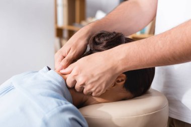 Masörün, bulanık arka planda esmer iş kadınına oturarak boyun masajı yaptığı görüntüler.