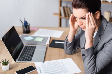 Migreni olan bir iş kadını anlaşmaların ve bilgisayarın yanında otururken yüzünü çeviriyor.