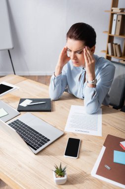 İş yerinde iş belgesi ve dijital cihazlarla oturan baş ağrısı olan kadın ofis çalışanı