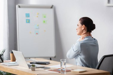İş yerinin yanındaki ofis sandalyesinde oturan boynu ağrıyan esmer iş kadını.