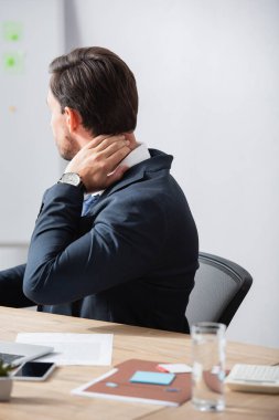 Boyun ağrısı çeken bir ofis çalışanı bulanık arka planda iş yerinde oturuyor.