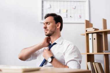 Boynu ağrıyan bir iş adamı iş yerinde ön planda bulanık bir masa ile oturuyor.