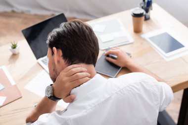 Boyun ağrısı olan bir ofis çalışanının arka planı bulanık arka planda oturuyor.