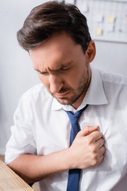 Ofiste göğüs ağrısından muzdarip olan ofis çalışanının görüntüsü bulanık arka planda