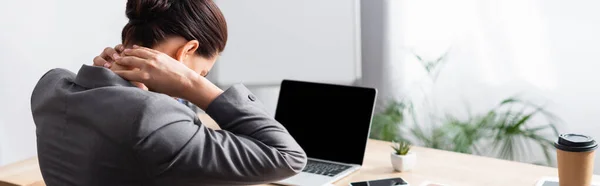 背景にぼやけた背景にノートパソコンで机に座って首を痛めている女性サラリーマンのバックビュー バナー — ストック写真