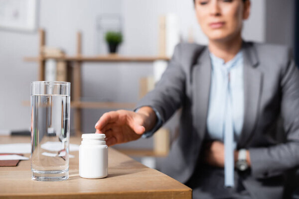 Cropped view of businesswoman with stomachache taking medication on blurred background