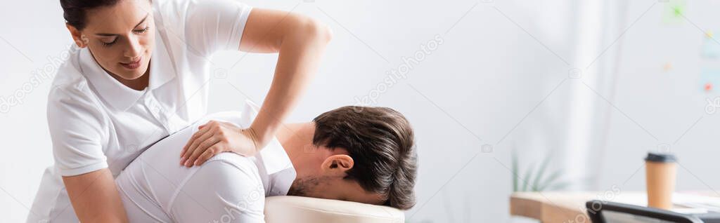 Positive masseur doing arm massage for client in office on blurred background, banner