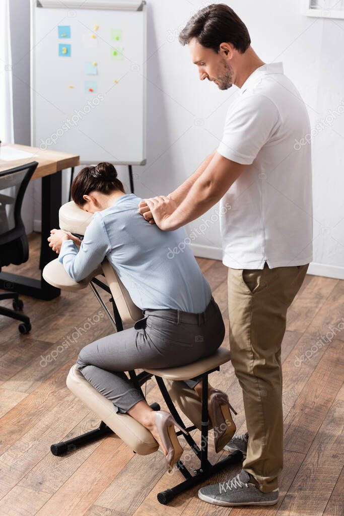 Massage therapist doing seated massage of back for businesswoman in office