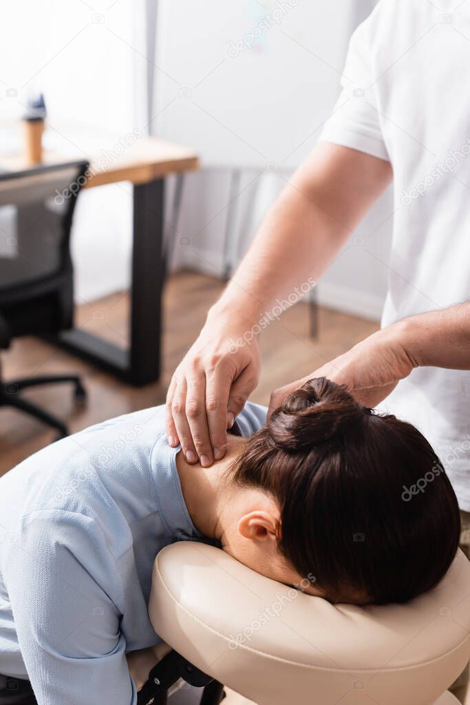 Massage therapist massaging neck of brunette businesswoman sitting on massage chair on blurred background