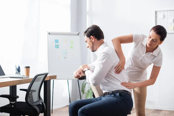 Masseuse doing seated massage of back for businessman in office