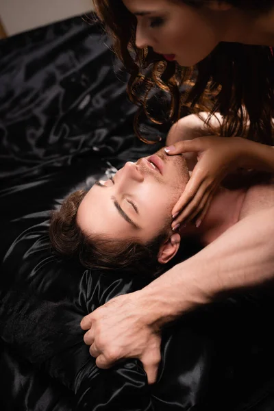 Young Woman Touching Chin Shirtless Boyfriend Closed Eyes Black Bedding — Stock Photo, Image