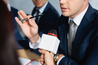 partial view of journalist with microphone interviewing politician during party congress on blurred foreground clipart
