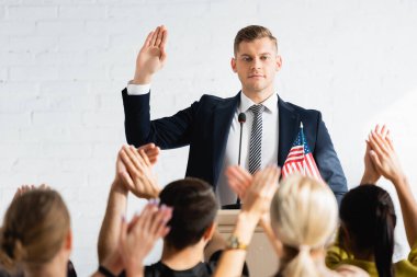 confident candidate showing swear gesture in front of applauding voters in conference room clipart