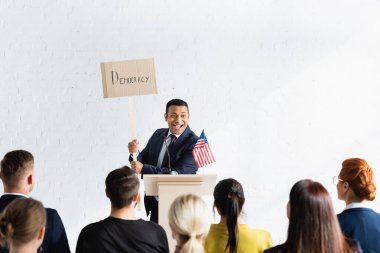 Konferans salonundaki seçmenlerin önünde üzerinde demokrasi yazılı pankart bulunan heyecanlı Hintli konuşmacı ön planı bulanıklaştırdı
