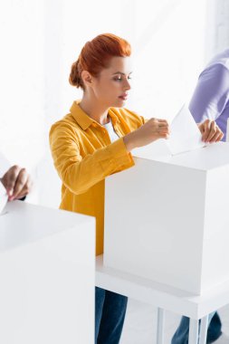 woman inserting bulletin into polling box near voters on blurred background clipart