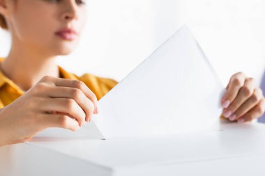 partial view of woman inserting ballot into polling box on blurred background clipart