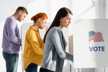 Amerikan bayrağı ve bulanık arkaplanda oy pusulası olan oy kullanma kabinlerindeki seçmenler
