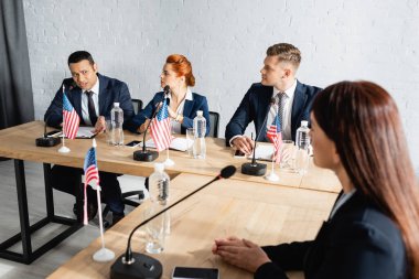 multiethnic politicians talking during party congress while sitting at desk with usa flags clipart