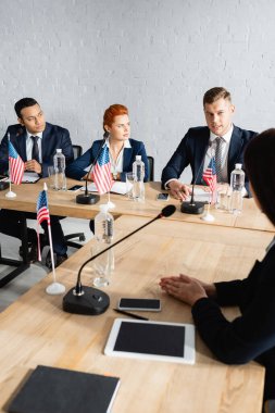 Parti kongresi sırasında ABD bayraklarıyla masaya otururken çok kültürlü politikacılar konuşuyor.