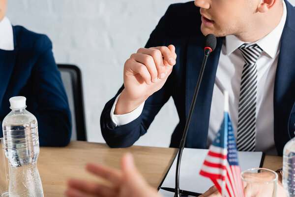 Обрезанный вид человека в формальной одежде жестом, во время разговора в микрофоне на размытом переднем плане