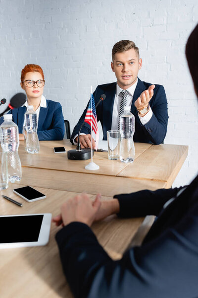 Политический жест, выступая в микрофоне и глядя на коллегу-женщину на размытом переднем плане