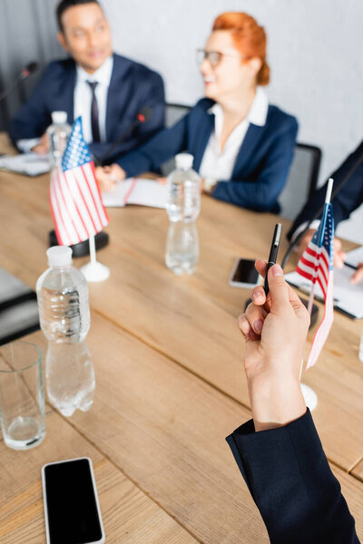 Man pointing with pen, while sitting in boardroom with blurred interracial colleagues