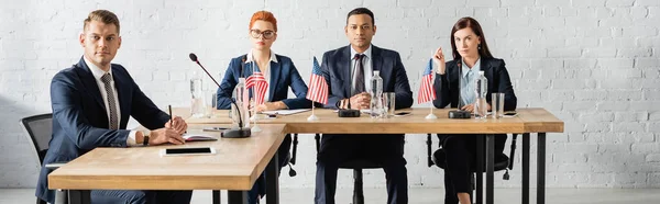 Political party members looking at camera, while sitting at table in boardroom, banner