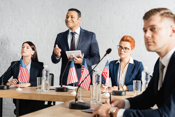 Счастливый индийский политик смотрит в сторону, стоя с цифровой табличкой рядом с коллегами в зале заседаний