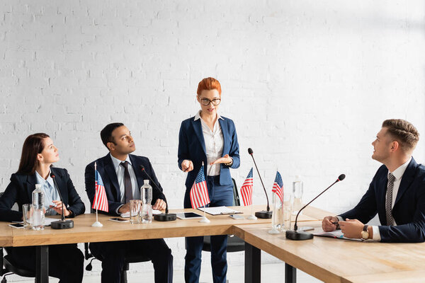 Politicians looking at smiling female colleague speaking, while standing in boardroom during political party meeting