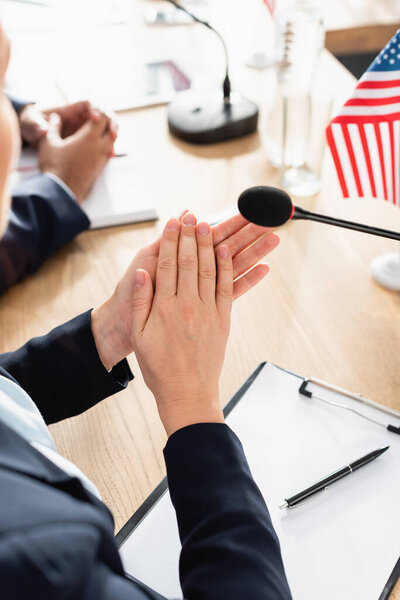 Обрезанный вид женщины в формальной одежде аплодирует, сидя возле буфера обмена с пустой бумагой и ручкой на размытом фоне