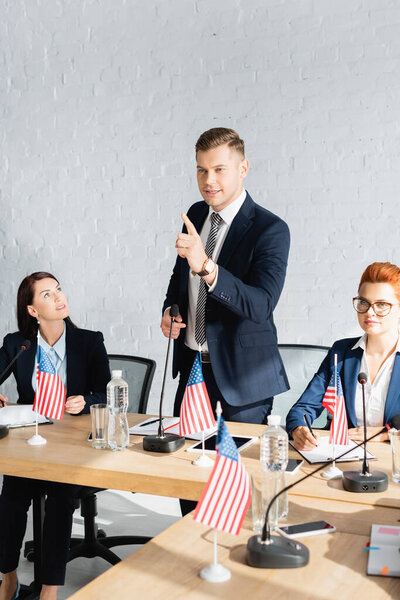 Smiling politician pointing with finger, speaking while standing near female colleagues during congress