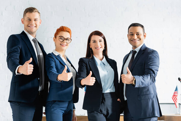 Smiling multicultural politicians with thumbs up looking at camera while standing in boardroom