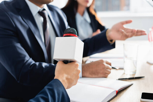 обрезанный взгляд журналиста на интервью с микрофоном политиком во время пресс-конференции на размытом фоне