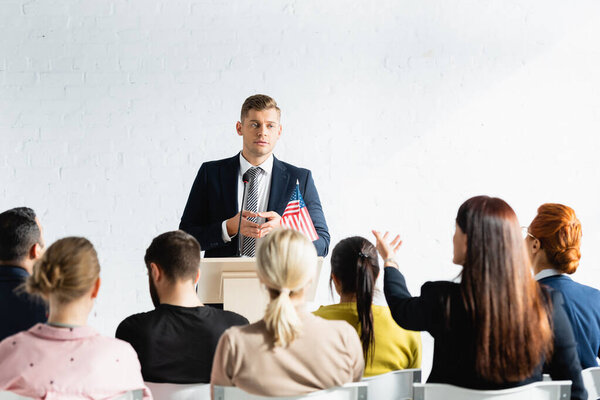 serious speaker standing in front of voters in conference hall, blurred foreground