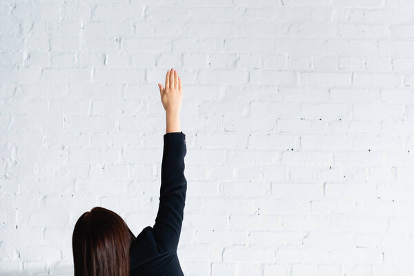back view of woman voting with hand in air against white brick wall
