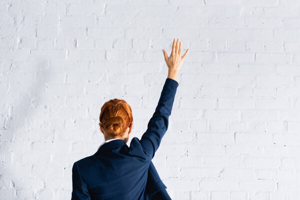 back view of woman voting with raised hand against white brick wall