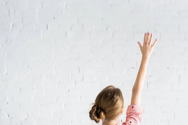 Achteraanzicht Van Vrouw Stemmen Met Opgeheven Hand Tegen Witte Bakstenen — Stockfoto