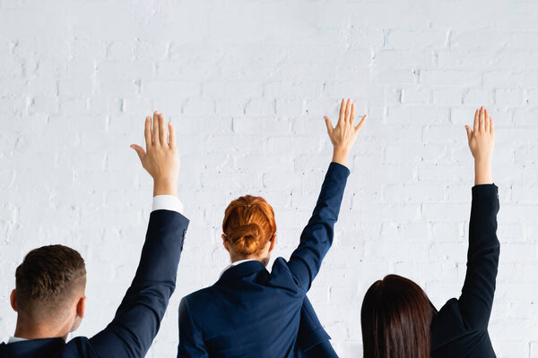 back view of women and man voting with hands in air against white brick wall