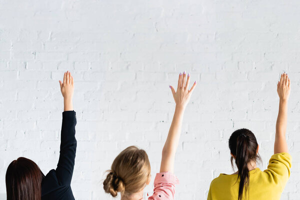 back view of women voting with raised hands against white brick wall