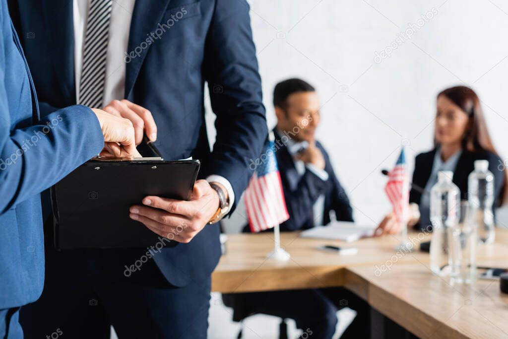 politician pointing with finger at clipboard while colleagues talking on blurred background