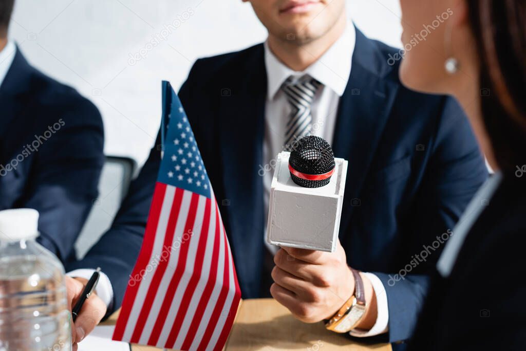 cropped view of correspondent with microphone interviewing politician during party congress, blurred foreground